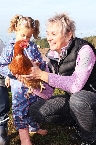 Vergrößerung des Bildes für Eine Frau und ein Mädchen streicheln ein Huhn.