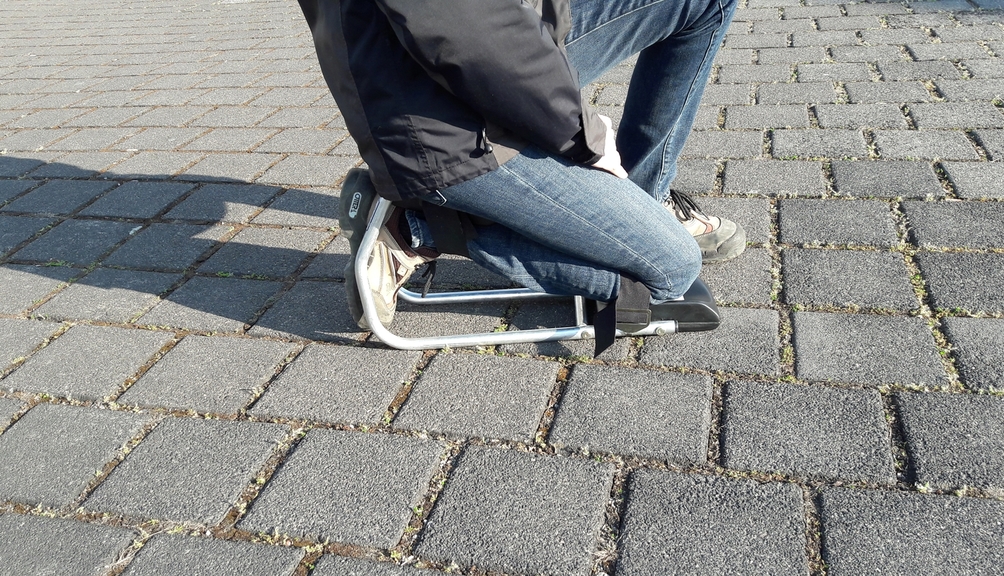 Vergrößerung des Bildes für Mensch demonstriert Kniehocker auf Straßenpflaster.