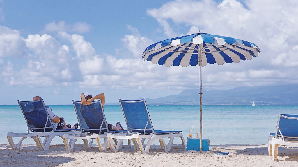 Vergrößerung des Bildes für Strand mit Liegestühlen und Sonnenschirm. Auf zwei Liegestühlen liegen Personen..