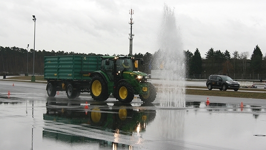 Traktor mit Anhänger fährt auf einer nassen Fahrbahn durch die Wasserfontäne