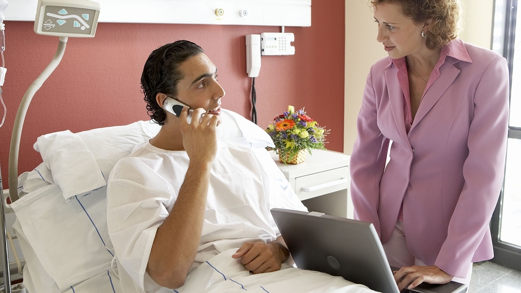 Frau mit Laptop berät Patient im Krankenhausbett