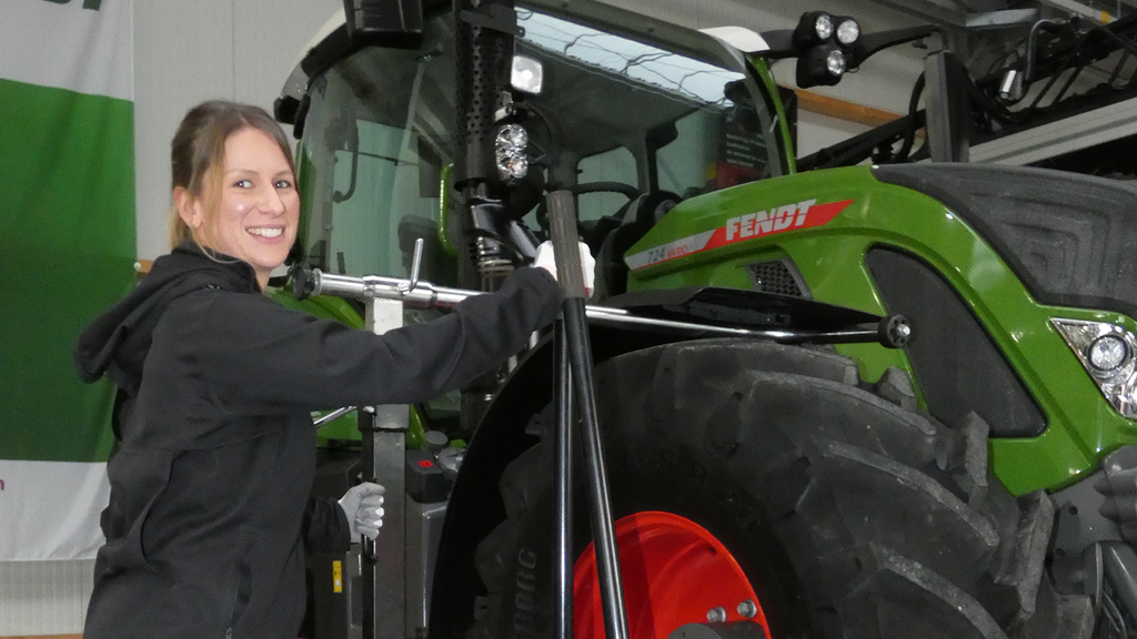 Vergrößerung des Bildes für Eine junge Frau in Arbeitskleidung steht vor dem Rad eines Traktors..