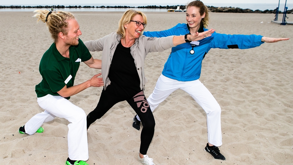 Zwei Frauen und ein Mann machen Yoga am Strand 