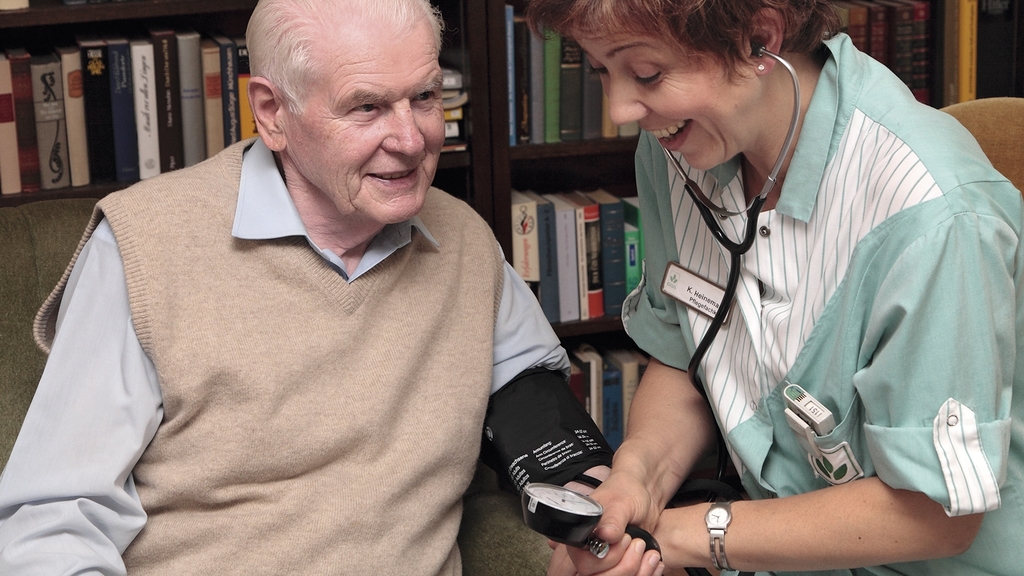 Vergrößerung des Bildes für Eine Pflegerin misst bei einem Senior den Blutdruck.
