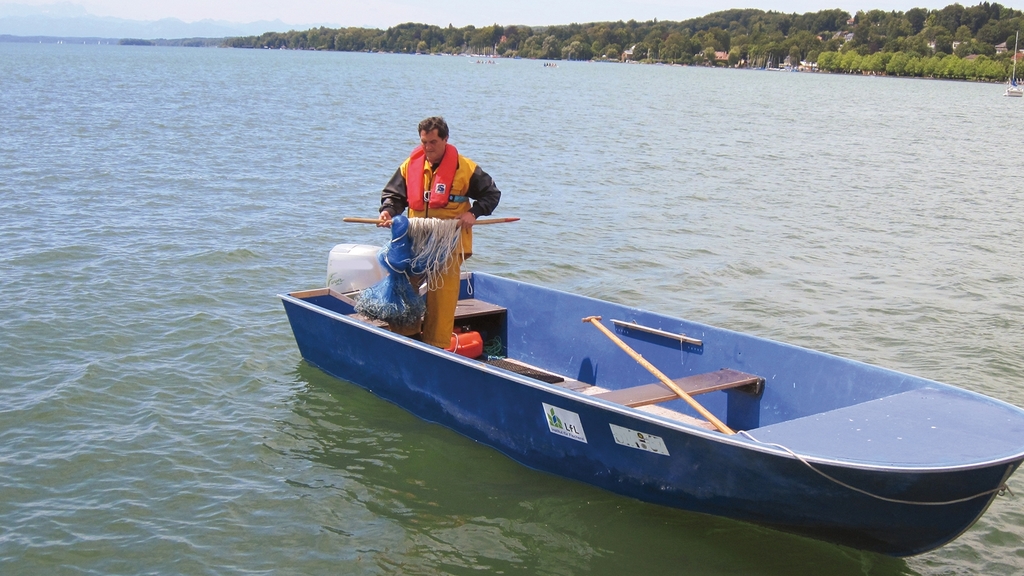 Vergrößerung des Bildes für Fischer steht auf einem kleinen Boot und zieht Fischernetze aus dem Wasser. .