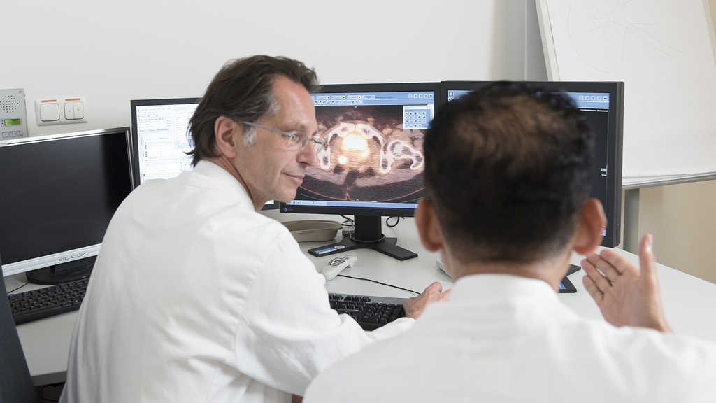 Ärzte beraten sich vor einem PC-Bildschirm. Auf dem Bildschirm ist ein medizinischer Scan zu sehen. 