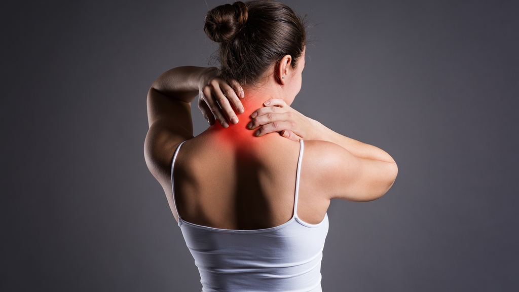Frau in Unterhemd und Rückenansicht fasst sich mit beiden Händen an den schmerzenden Nacken. Nackenpartie ist rot markiert, was die brennenden Schmerzen bildlich darstellen soll.