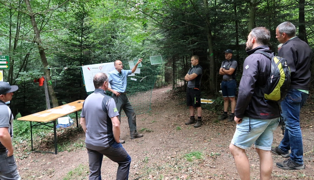 Vergrößerung des Bildes für Bild: Mann erklärt mehreren Personen die Station Arbeitsauftrag im Wald.